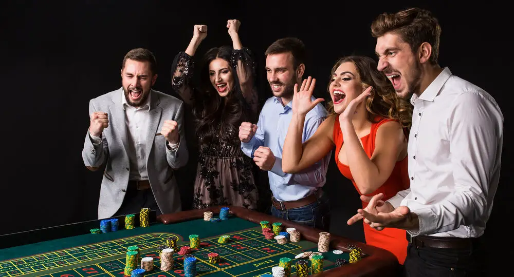 Group,Of,Young,People,Behind,Roulette,Table,On,Black,Background